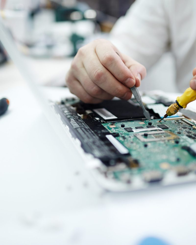 Closeup shot of unrecognizable man fixing circuit board in laptop using screwdriver and different tools on table in workshop